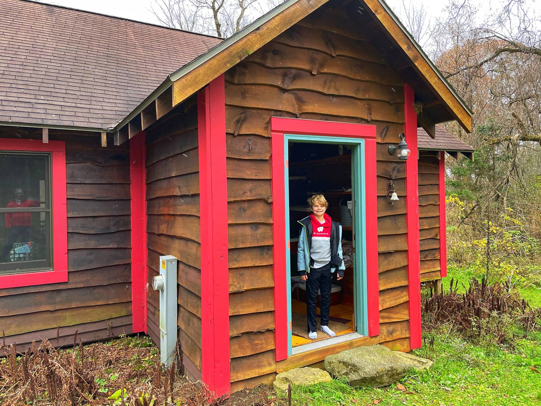 A boy standing in the doorway of a red-trimmed cabin