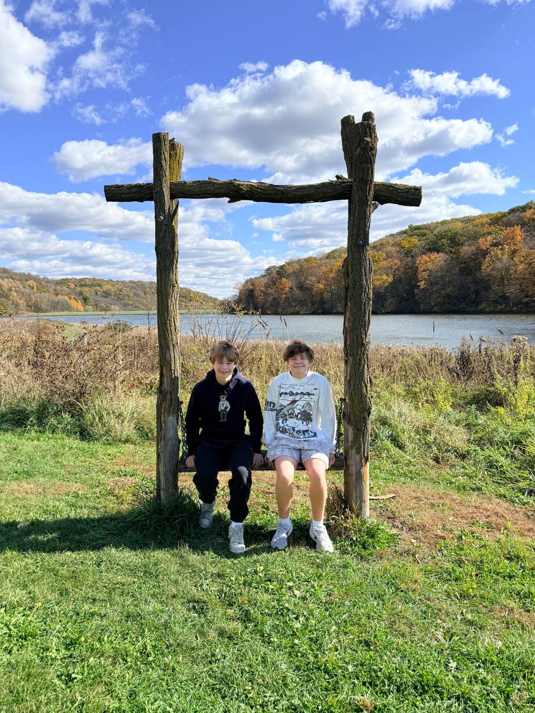 Two children on a log swing beside a lake in autumn