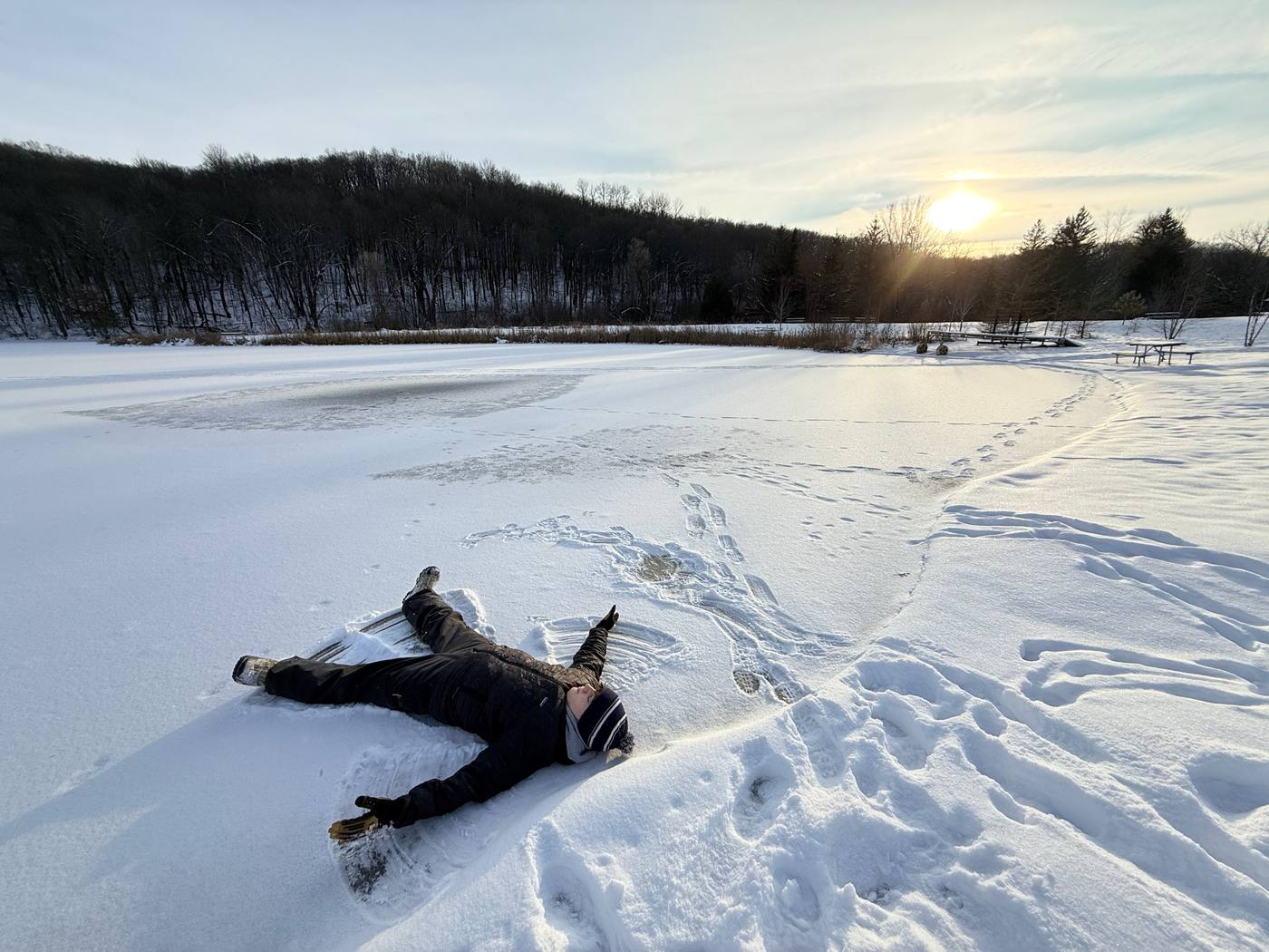 A child making a snow angel on a frozen pond below a wooded ridge